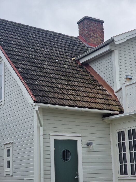 Gammalt hus med tak täckt av gamla betongpannor, diskussion om att byta till liknande takpannor. Vit fasad och röd tegelstensskorsten.