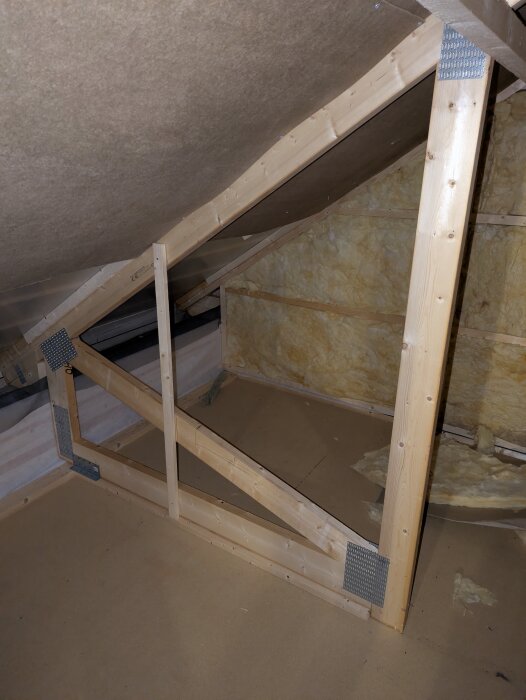 Modifierad takstol med träreglar, en snedsträva och metallförstärkningar i ett oinrett vindsutrymme under konstruktion.