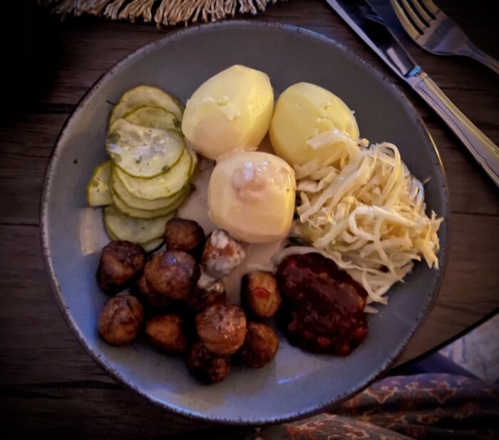 Tallrik med köttbullar, potatis, sås, lingonsylt, stekt vitkål och inlagd gurka.
