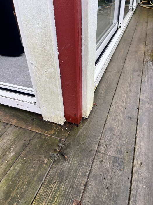 Hörn av uterummet med fukt runt trätrallar och en röd pelare. Vitmetallen längs golvet i hörnet har kondens, och det är byggt i nivå med yttertrallen.