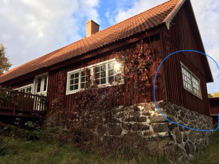 Rött hus med tegelpannor, stenfot och vita fönster. Blå markering kring fönster på gavelplan där glasveranda planeras.