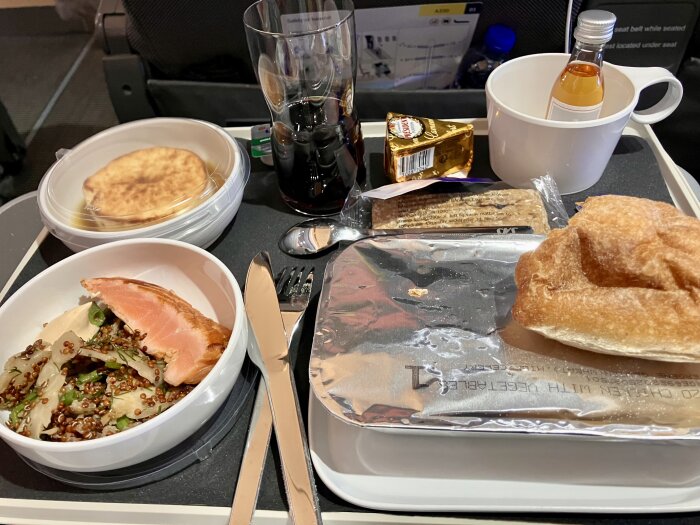 Matbricka på ett flygplan med lax, quinoa, bröd, kex, smör, en liten whiskyflaska och en drink.