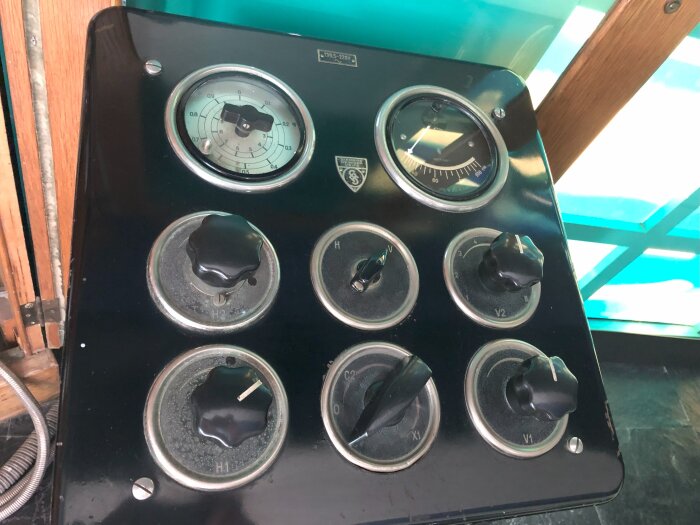 Manövertavla till gammal röntgenapparat med diverse rattar och mätare, monterad på en svart panel med trädetaljer i bakgrunden.