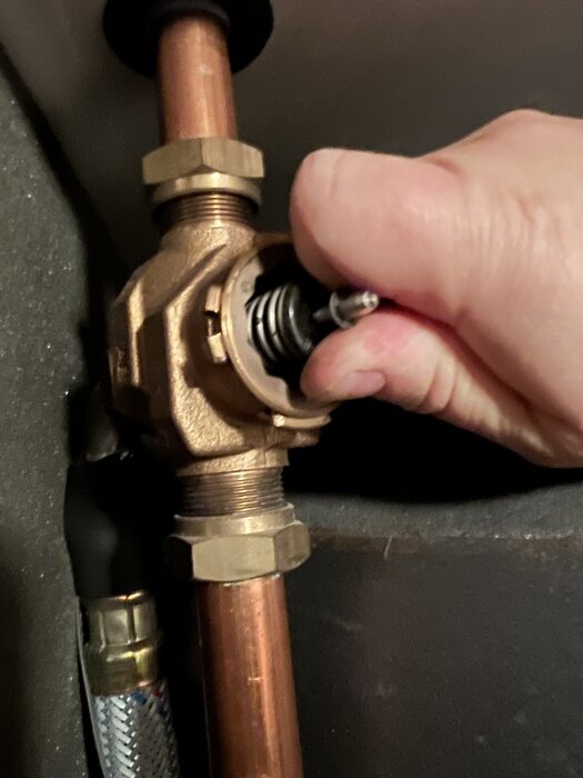 Hand trycker på fjädern i en växelventil monterad på ett kopparrör. Ventilen är öppen och mekanismen undersöks för problem.