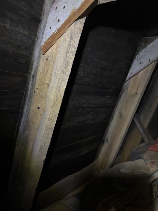 Bijälk och takbjälkar med svartnande råspont och mjölsäckar i ett vindsutrymme.