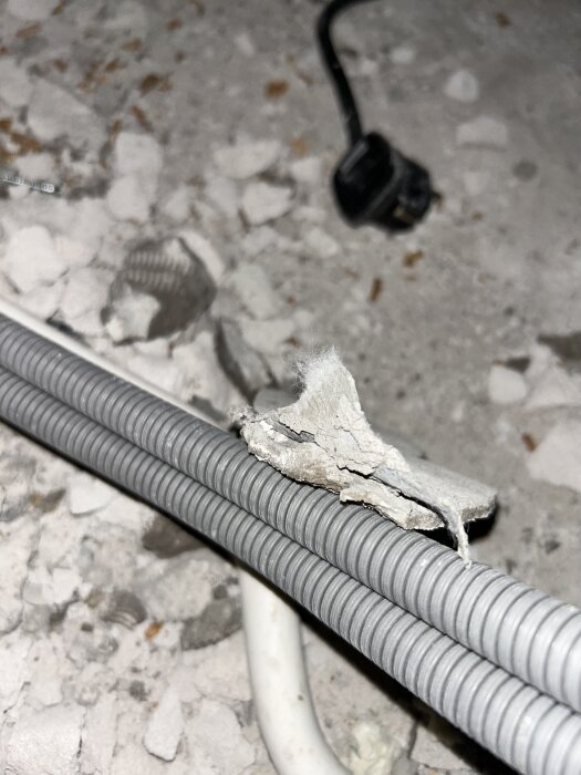 Sladdar och lös bit gipsliknande material med vita fibrer på ett badrumsgolv under renovering. Bakgrunden visar en strömkabel.