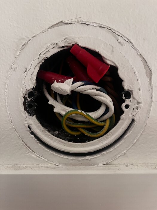 Elinstallation med synliga kablar i en dosa; kablarna löper uppifrån och snett uppifrån, med röd och gul och grön isolering i bakgrunden.