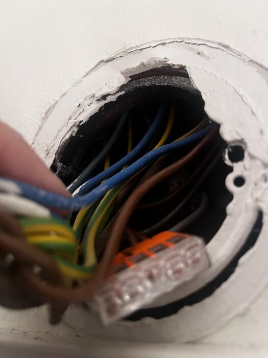 Närbild av en elektrisk dosa med flera färgade kablar och en kopplingsklämma synlig inuti.