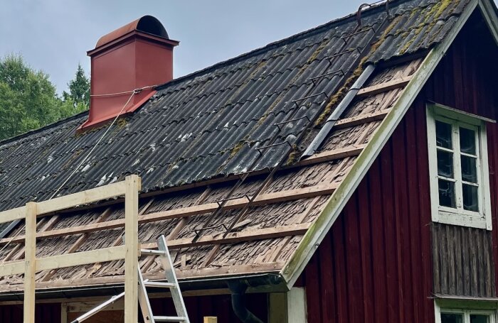 Ett äldre rött hus med takrenovering på gång, där bärläkt är synlig under en delvis borttagen takbeklädnad.