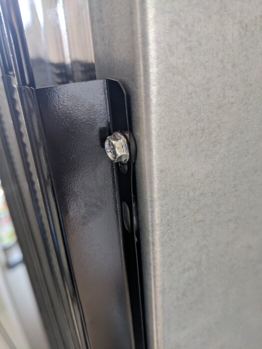 Närbild på en metallbricka med skruv och gummiring monterad på ett kylskåp för att minska vibrationer och ljud.