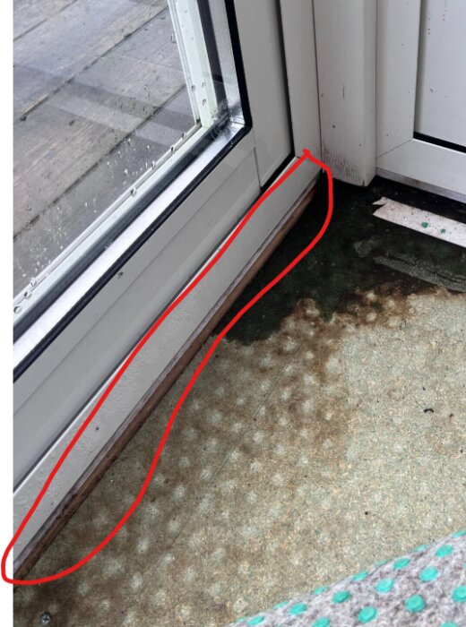 Fuktfläck på golvspånskiva vid dörrkarm, indikerar potentiell läcka; röd markering visar området där trallbrädan möter spånet.