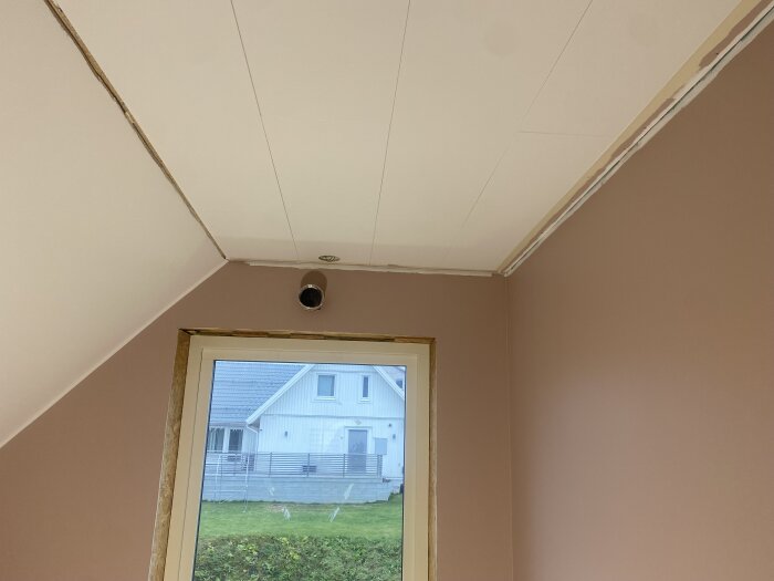 Snedtak med två vinklade hörn och taklist, fönster mot trädgård och grått hus.