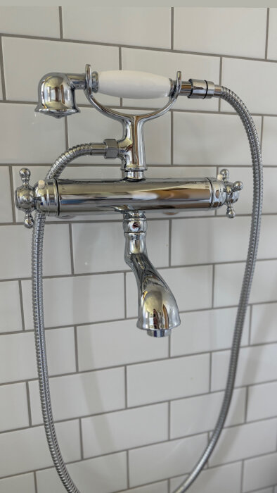 Kromad duschblandare installerad mot väggen med vitt kakel i ett nyrenoverat badrum.