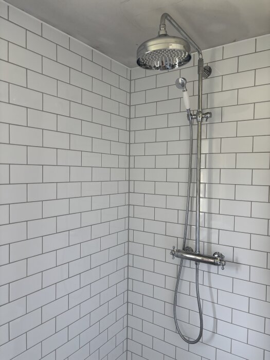 Dusch med vitt kakel och kromad regndusch samt handdusch i ett nyrenoverat badrum.