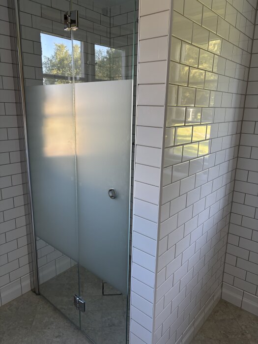 Duschhörna i badrum med vitt kakel och frostad glasdörr, del av renoveringsprojekt.