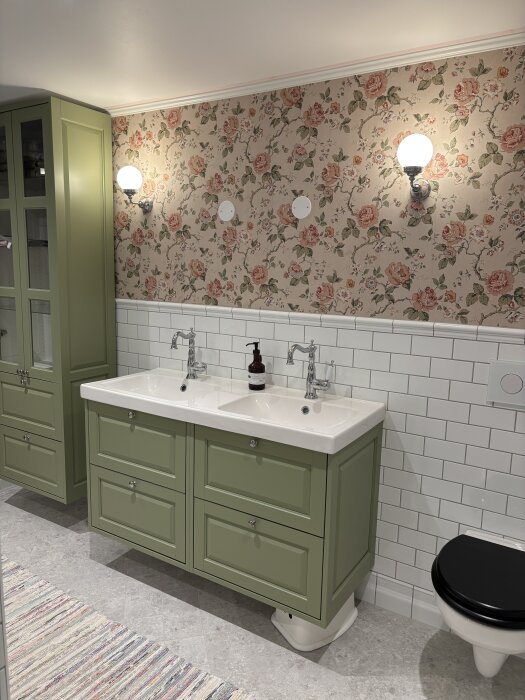 Badrum med gröna möbler, blommig tapet och dubbla handfat.
