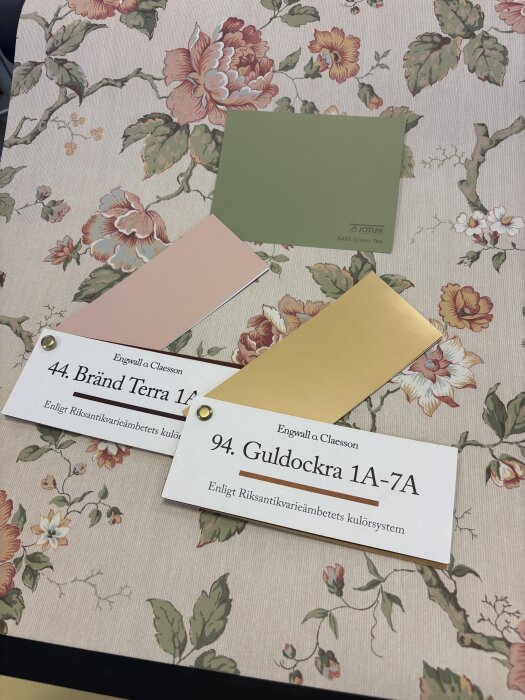 Färgguider för inredning: Grönt, rosa och guldockra färgprover på blommigt tapetmönster.