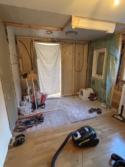 Renovering av badrum med verktyg på golvet, dammsugare och kattlåda i ett halvklart utrymme.