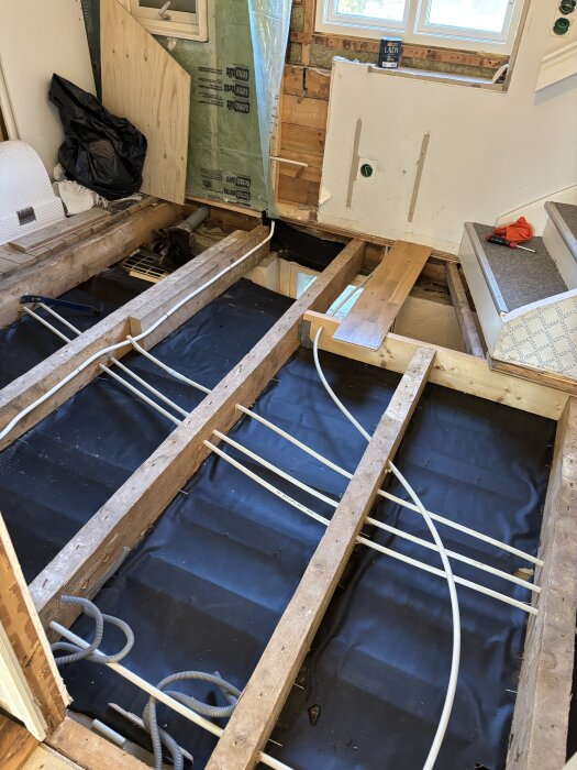 Golv under renovering med exponerade bjälkar och rör för vattenburen värme, redo för installation i ett ombyggt badrum.