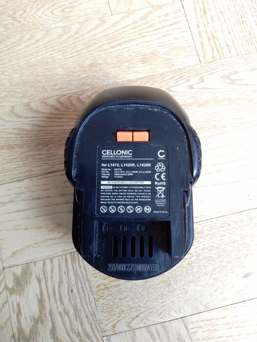 Bilden visar ett svart Cellonic-batteri med etikett och information för modellerna L1415, L1420R, L1430R, liggande på ett ljust trägolv.