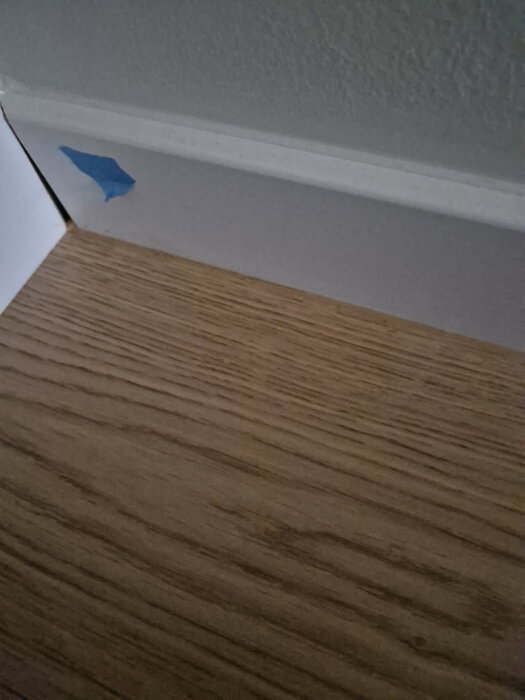 Byggnation av sockel med trägolv och blå tejp på väggen.