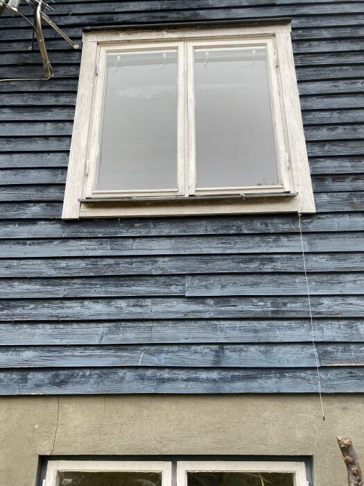 Fönster på en byggnad med blå fasad och sliten träpanel.