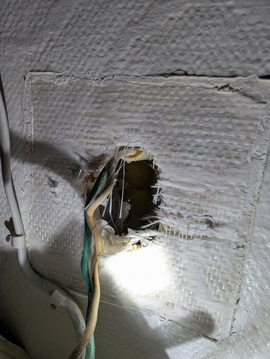 Exponerade kablar och trasigt hål i en vägg, med skadat isoleringsmaterial runt omkring.