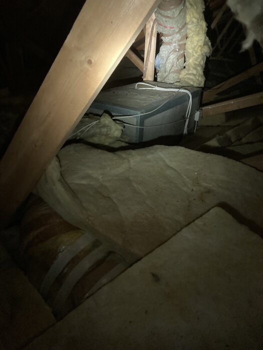 Isolerade ventilationsrör och glasull på vinden. Detalj av ventilationssystemet (FTX) med isolering runt rören, synliga bjälkar.