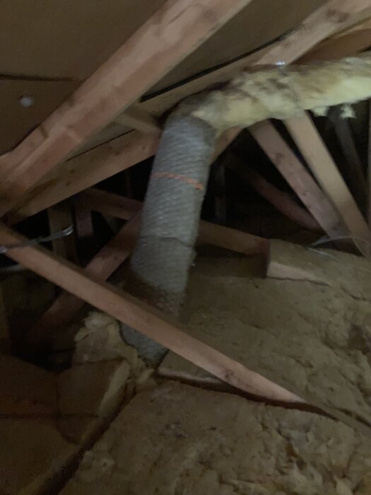 FTX-ventilationsrör i vinden med delvis exponerad isolering av glasull på golvet, inramat av träbjälkar.