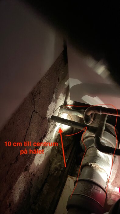 Närbild av avloppsrör och koppling i ett väggutrymme, med markerad text som anger '10 cm till centrum på hålet'.