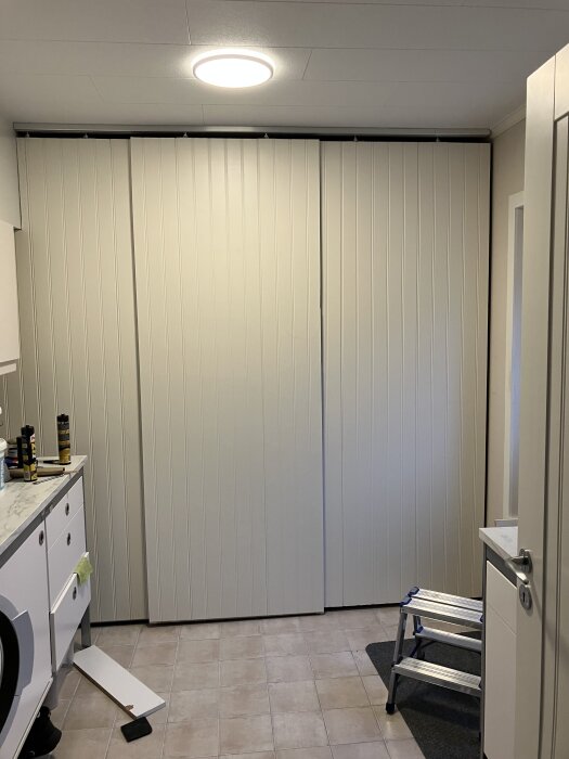 Tre vita skjutdörrar monterade i ett rum, med verktyg och en stege i närheten, färdigmålning planeras senare.