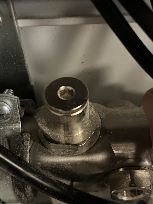 Metallock med insexhål, troligen del av ventil, nedsmutsat och omgiven av kablar och rör.