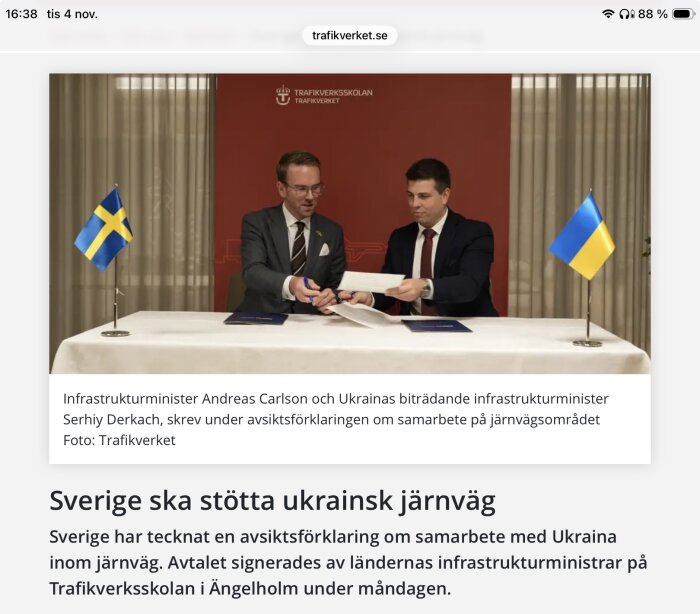 Två personer signerar dokument vid bord med svenska och ukrainska flaggor i bakgrunden.