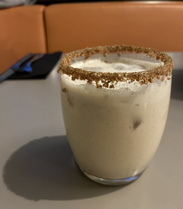 Kall krämig dryck i glas med kanelkantsdekoration på ett bord med orange bakgrund.