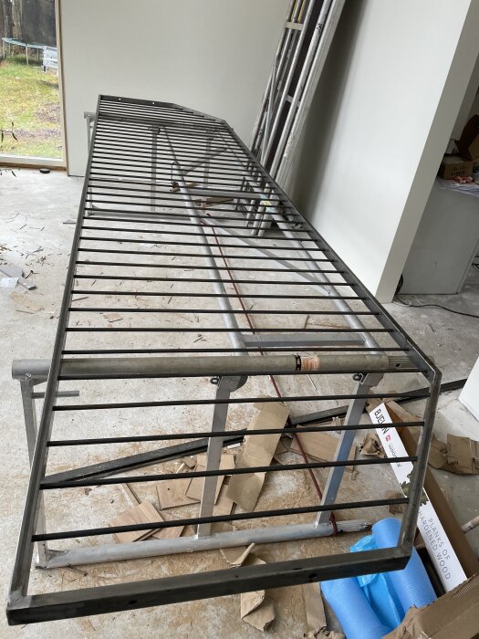Stort metallstaket inomhus, nyss klart efter svetsning. Ramar av metallrör, placerat på betonggolv med byggmaterial i bakgrunden.