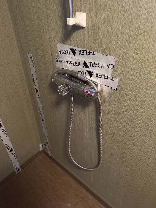 Badrumsvägg med vattenrör i koppar täckta med T-FLEX tejp och en slangen till en dusch.
