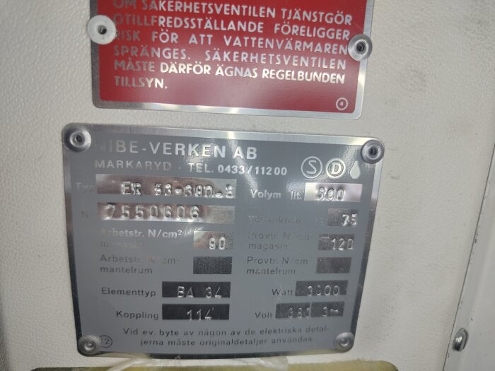 Skylt på Nibe-anordning med tekniska specifikationer som visar typnummer, serienummer och information om elementtyp och volym.