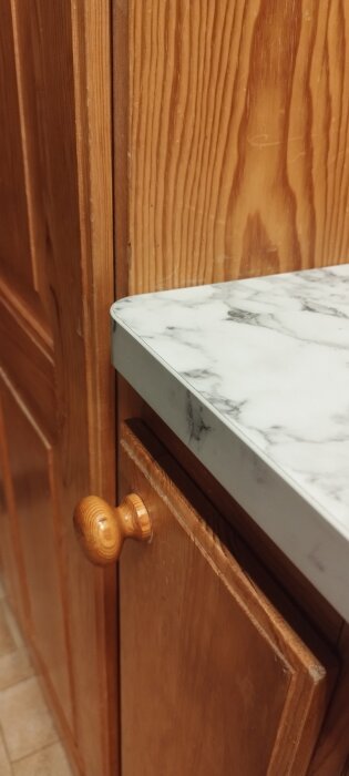 Köksbänk med vit marmorerad bänkskiva ovanför träskåp och trähantag.