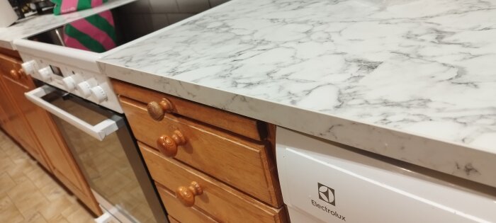 Måttbeställd marmormönstrad bänkskiva i kök med träskåp och Electrolux diskmaskin.
