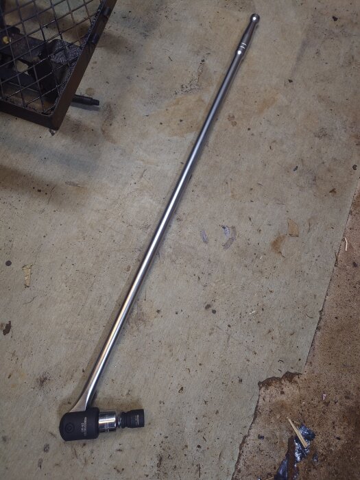 3/4 ledhandtag med hylsa på ett betonggolv, bredvid ett metallgaller.