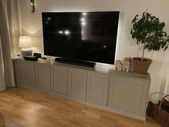 Grått skåp av MDF i vardagsrum med TV, bordslampa och grön växt, byggt med IKEA-skåp och tryckknappar istället för knoppar.