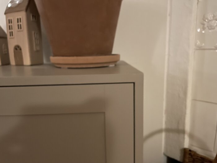 En beige IKEA-möbel klädd i MDF, med en terrakottakruka ovanpå. Små husdekorationer syns i bakgrunden.