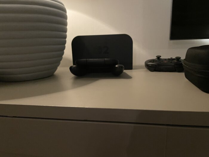 IKEA-skåp klädd i MDF med föremål ovanpå, inklusive en controller och en datorenhet, bredvid en randig kruka.