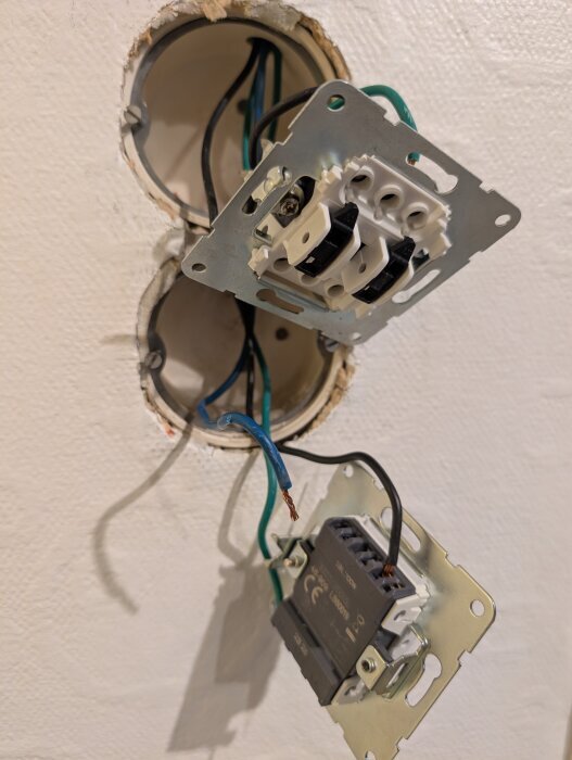 Två eluttag med kablar lossnade från väggen, med synliga svarta och gröna kablar i en dubbel eldoscentral.