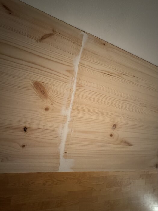 Träpanel av furu med synliga ådringar och en skarv, del av ett hemmabygge där plankorna är sammanfogade och slipade för att bli målade.