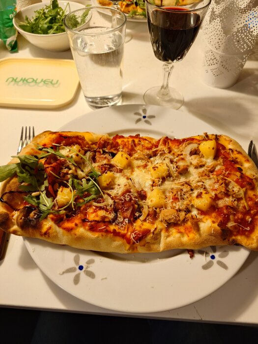 Hemlagad pinsa halvt toppad med prosciutto, rucola, pinjenötter, balsamico och halvt med tonfisk, lök, samt ananas på båda sidor.