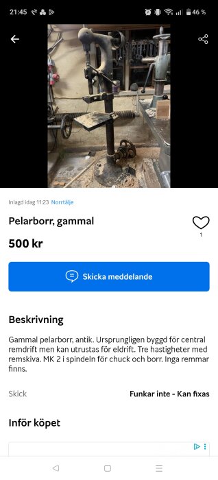 Gammal pelarborr med damm på, omgiven av verktyg i en sliten verkstad. Borrmaskinens bord är täckt av sågspån.