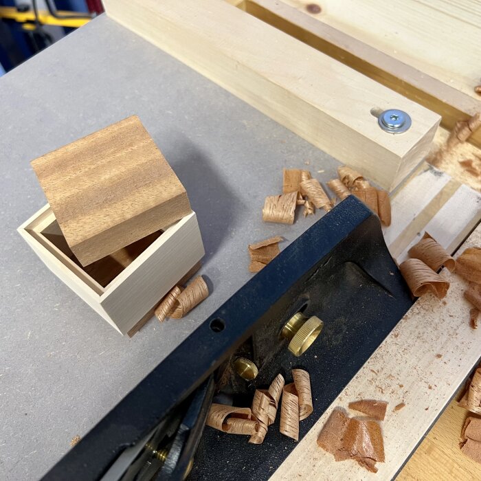 Handgjord trälåda på arbetsyta med hyvlat träspån och hyvel i träverkstad.