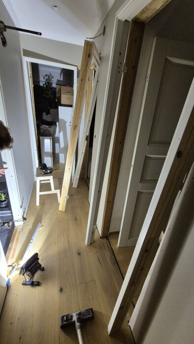 Renovering pågår i hall med nymonterade dörrkarmar, parkettgolv och byggmaterial samt verktyg utspridda på golvet.