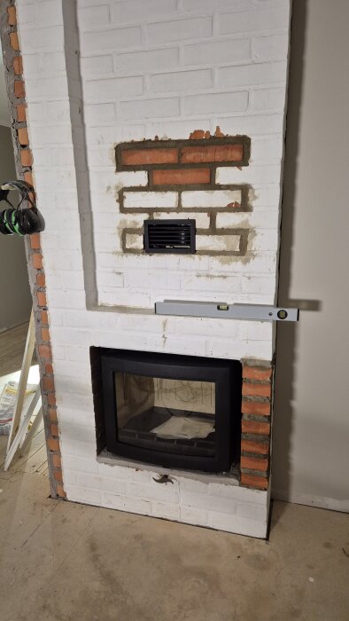 Insatsrör och kamin installerad i en murstock av tegel och puts. En vattenpass ses ovanpå kassetten under byggprojektet.